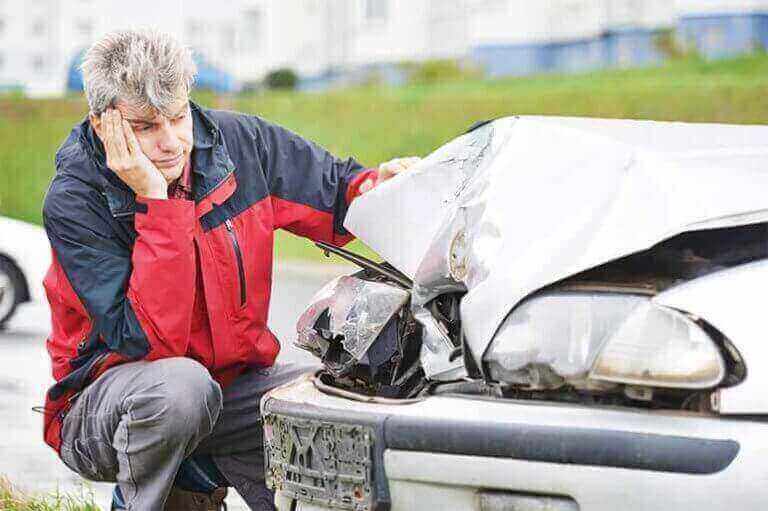 sad man looking at car accident damage