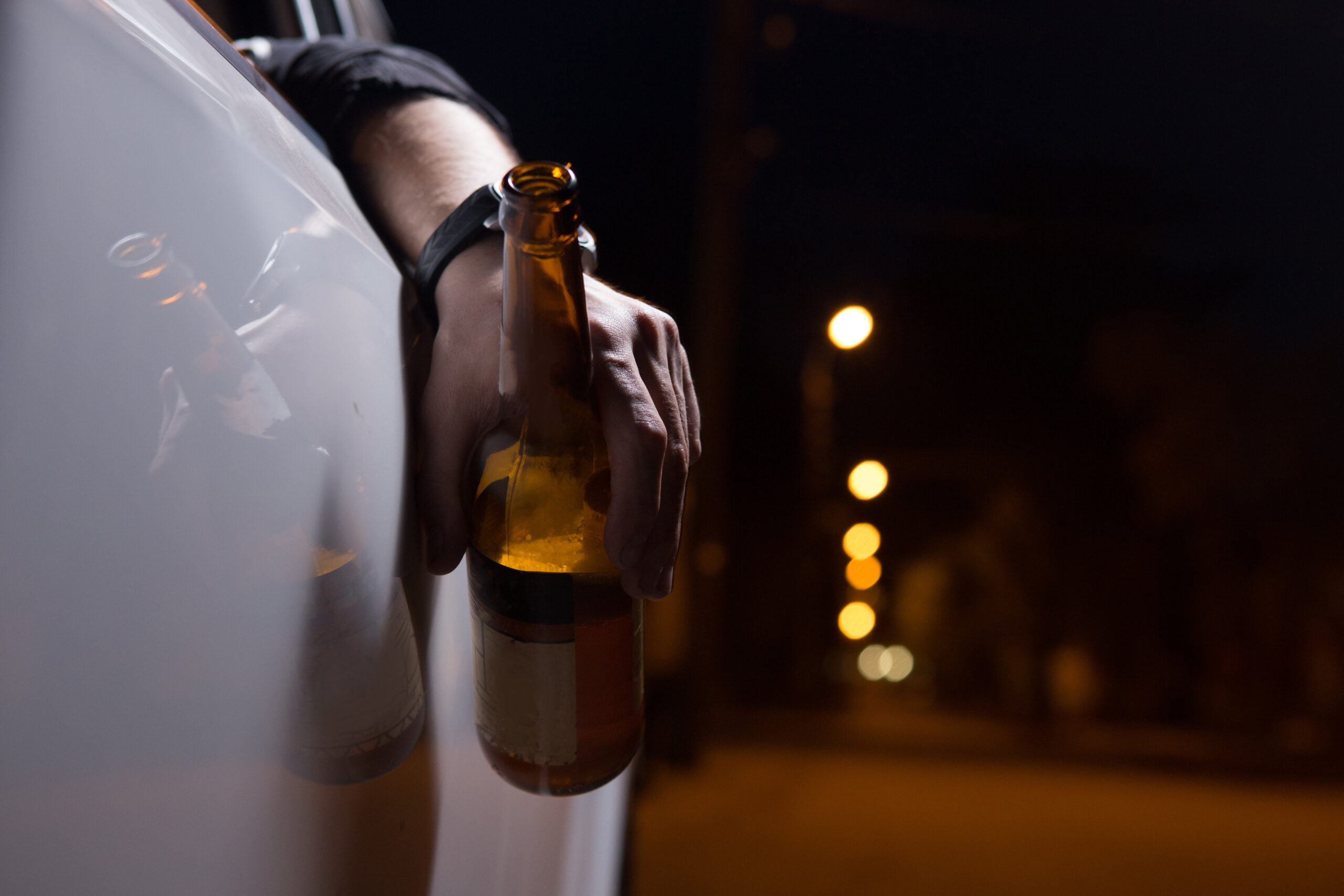 picture of a hand with a bottle of beer outside of a car door.