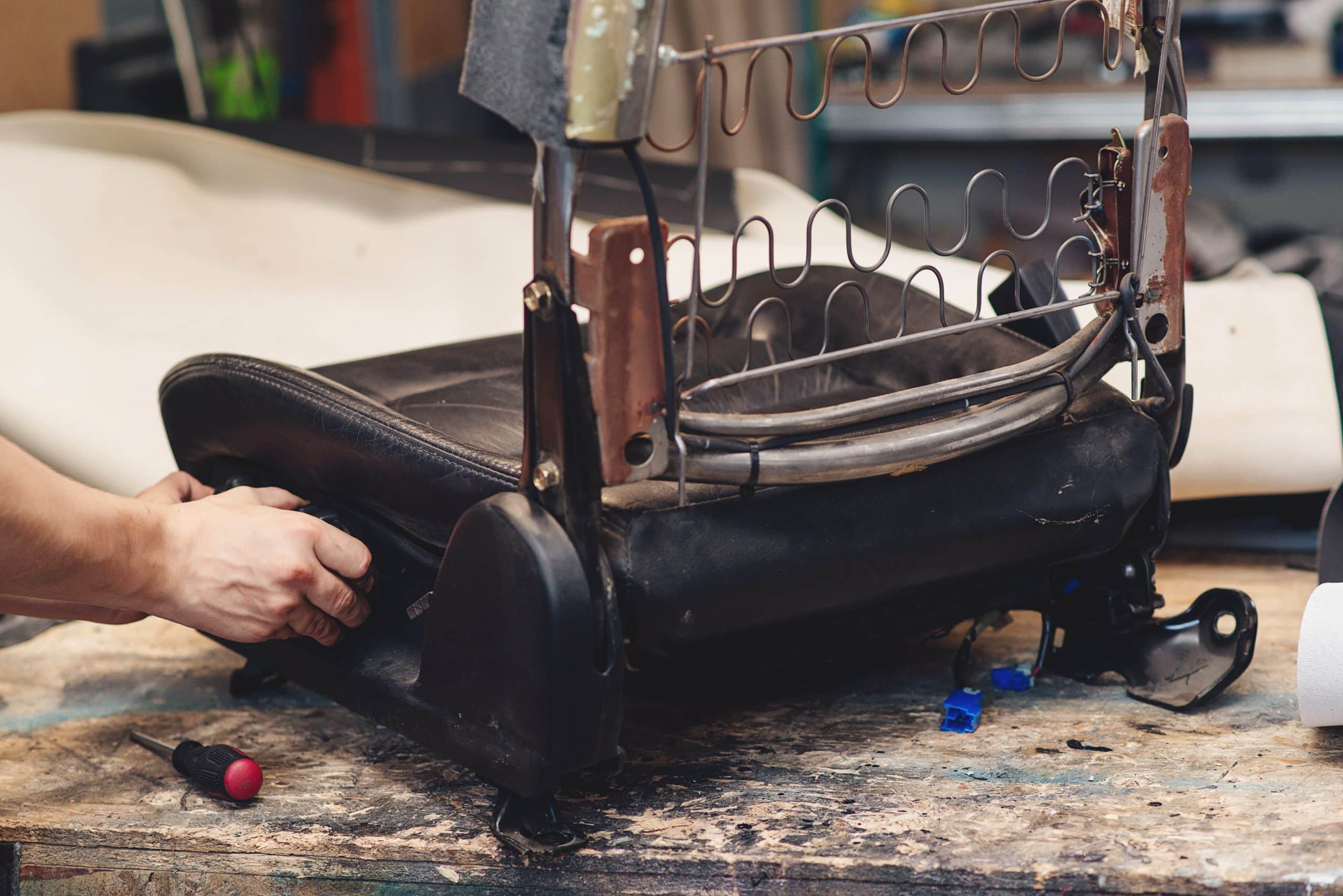 A mechanic works on a car seat frame.