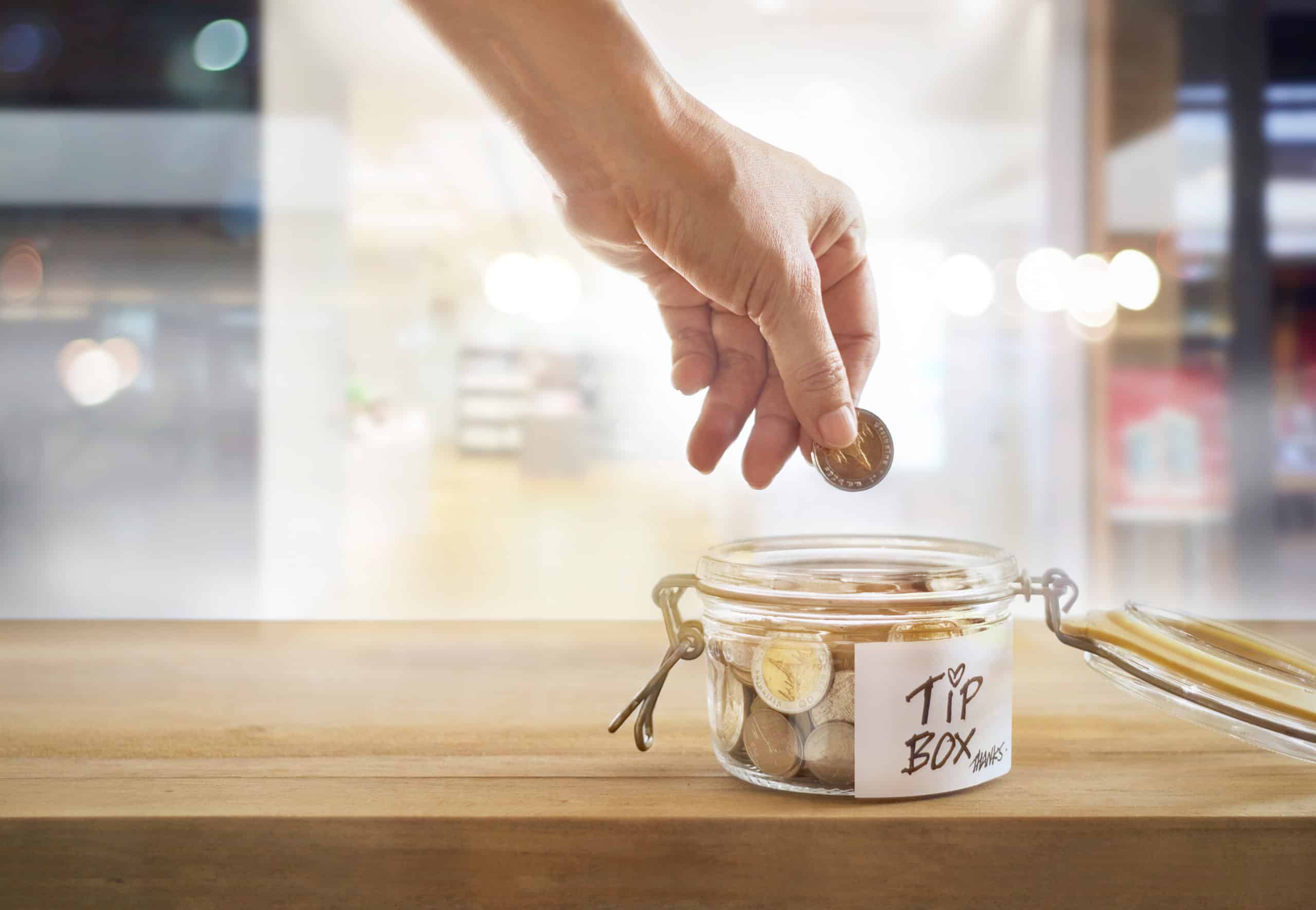 A customer puts tips into a jar for pooling tips.