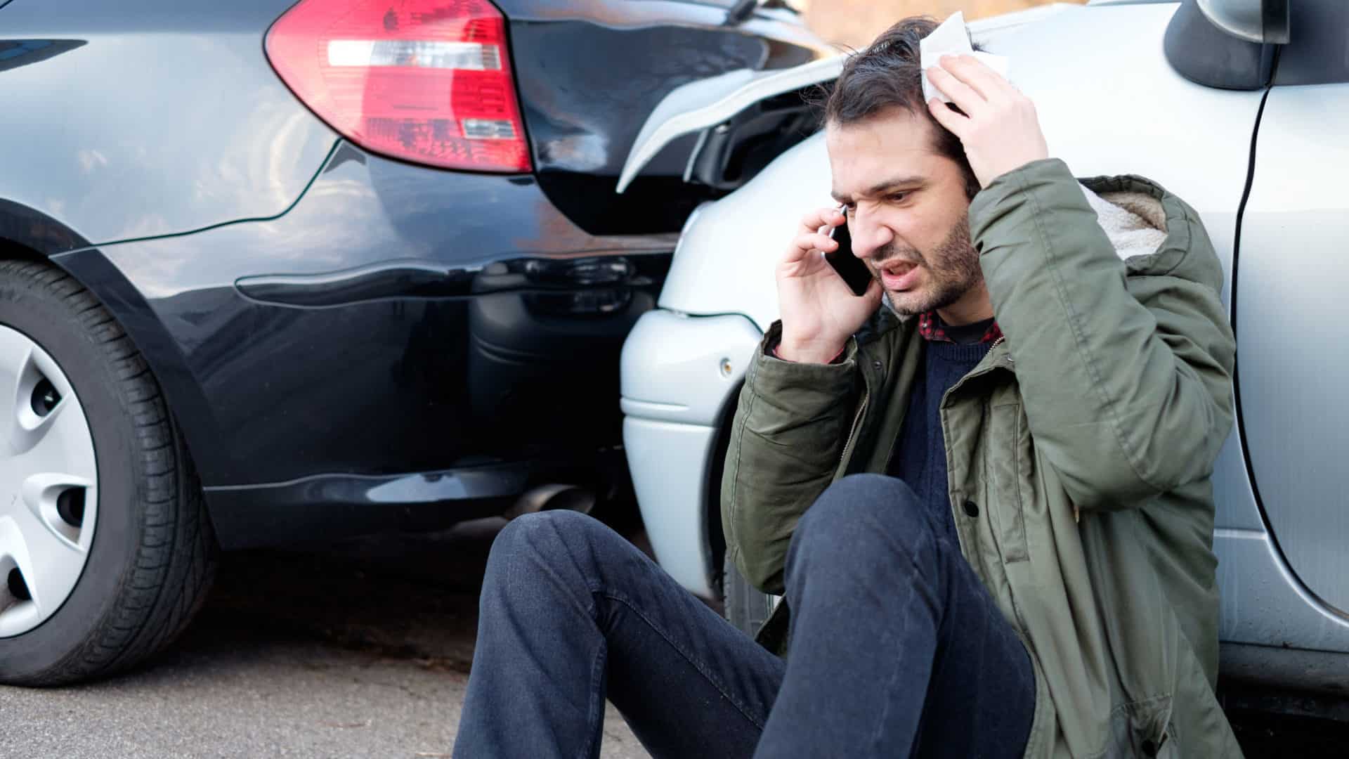 man calling the police on his cellphone after a car crash