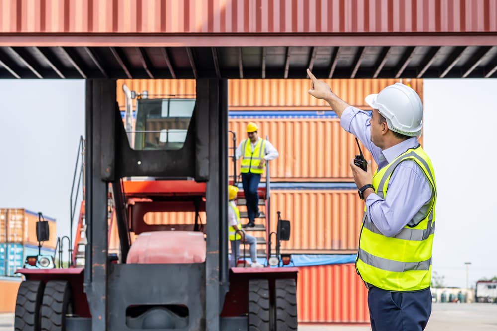 A manager on radio communication to control container load in industrial in front of machine lift container and cargo space. transport and logistics concepts.