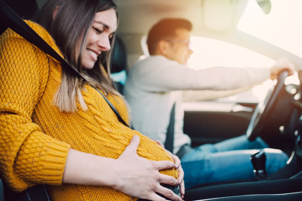 Pregnant with contractions in a car, her concerned husband driving. Preparing for childbirth on the go.