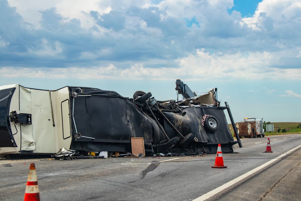 Overturned black truck on highway with emergency cones.