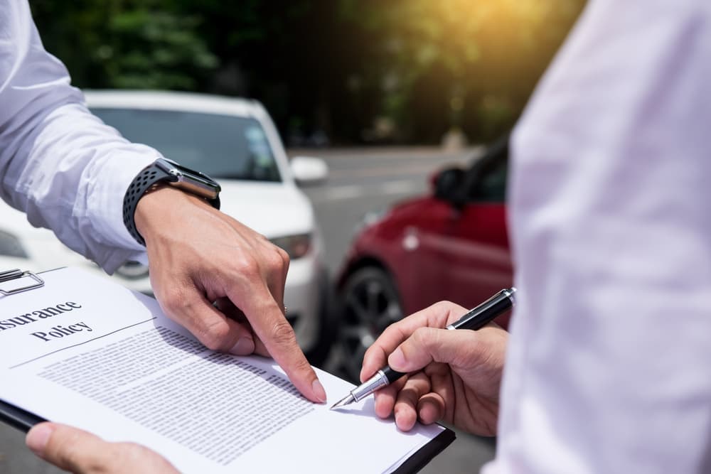 Insurance agent assessing and processing car accident claim, writing on clipboard.