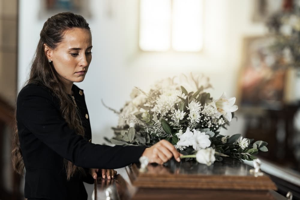 Woman placing flower on coffin at funeral, expressing grief, mourning, and sadness for loss of loved one.