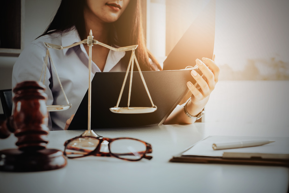 Business woman and lawyers discussing contract papers with brass scale on wooden desk in office.